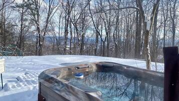 A hot tub outdoors surrounded by snow-covered ground and leafless trees.