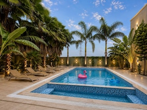 Una piscina con sillones de descanso y palmeras.