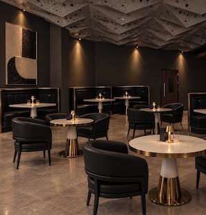 Interior moderno de restaurante con mesas redondas, asientos de cuero negro y un diseño de techo perforado único.