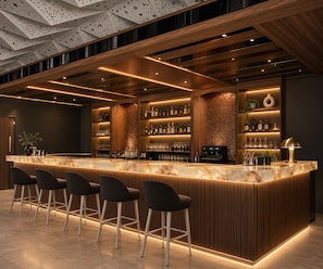 Un área de bar moderna con mostrador de mármol, taburetes y una variedad de botellas y vasos.