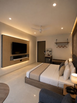 Een moderne hotelkamer met een groot flatscreen televisietoestel aan de muur, een bed met hoofdeinde, nachtkastjes, een bureau en een plafondventilator.