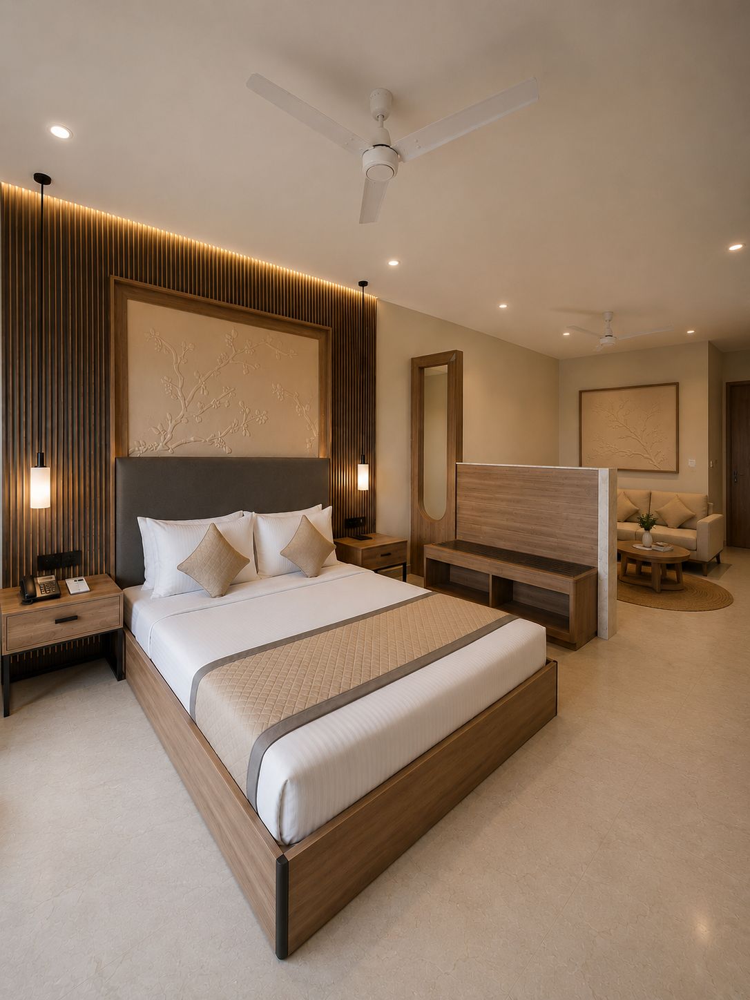 Un dormitorio moderno con una cama grande, mesitas de noche, una mesita auxiliar, un cabecero de madera, ventilador de techo y una zona de estar con sofá y mesa de centro.