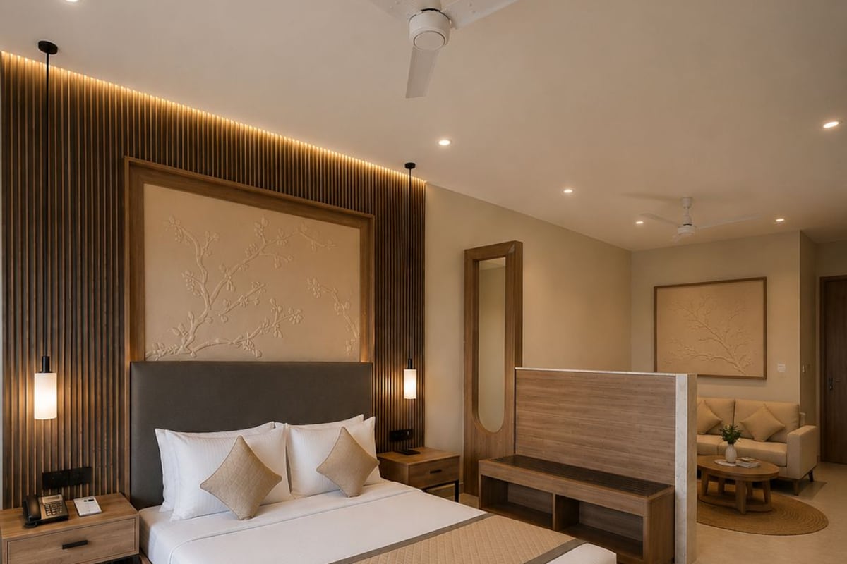 Un dormitorio moderno con una cama grande, mesitas de noche, una mesita auxiliar, un cabecero de madera, ventilador de techo y una zona de estar con sofá y mesa de centro.