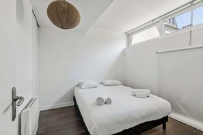 A bedroom with a bed, pillows, a window, and a ceiling light fixture. - Cozy 2-Bedroom House by Made For You (Neuilly-sur-Seine)