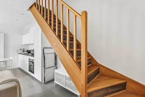 A modern kitchen with white cabinetry, a wooden staircase with a metal handrail, and a white chair. - Cozy 2-Bedroom House by Made For You (Neuilly-sur-Seine)