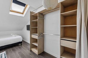 Ein Schlafzimmer mit einem Bett, einem Kleiderschrank mit vielen Regalen, einer Kleiderstange und einem kleinen Fenster.