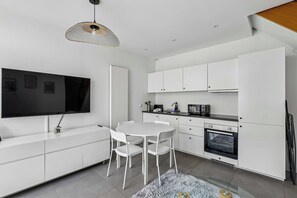 Una cocina moderna con muebles blancos, una mesa de comedor con sillas, horno empotrado y televisor de pantalla plana en la pared.