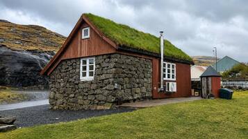 A stone building with a grass roof and wooden walls, located near a body of water with a cloudy sky.