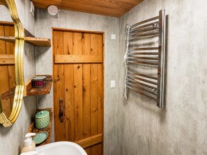 Un baño con puerta de madera, perchero, repisa con artículos de aseo y espejo.