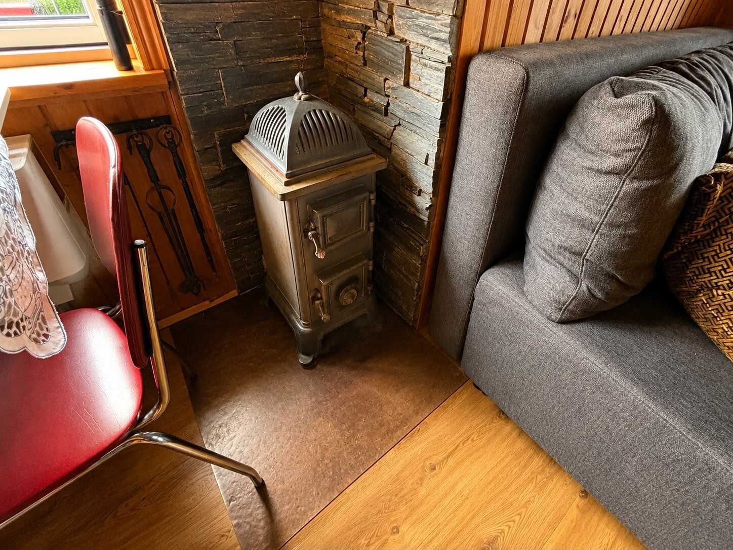 Un coin douillet avec un fauteuil rouge, un poêle ancien et un canapé gris agrémenté de coussins à motifs.