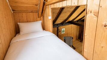 A wooden room with a bed, a chair, and a visible door leading to another space.
