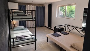 Una habitació de dormitori amb lliteres, un llit individual, una finestra amb vista a vegetació i un escriptori amb cadira.