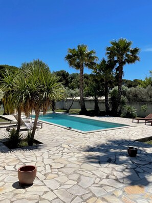 Una piscina amb paviment de pedra, envoltada de palmeres i un cel blau clar.
