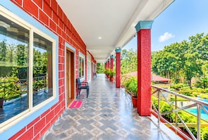 A covered corridor with red brick walls, potted plants, and a pool in the background.