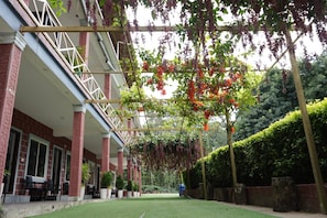 A covered outdoor area with a brick building, potted plants, and hanging plants.