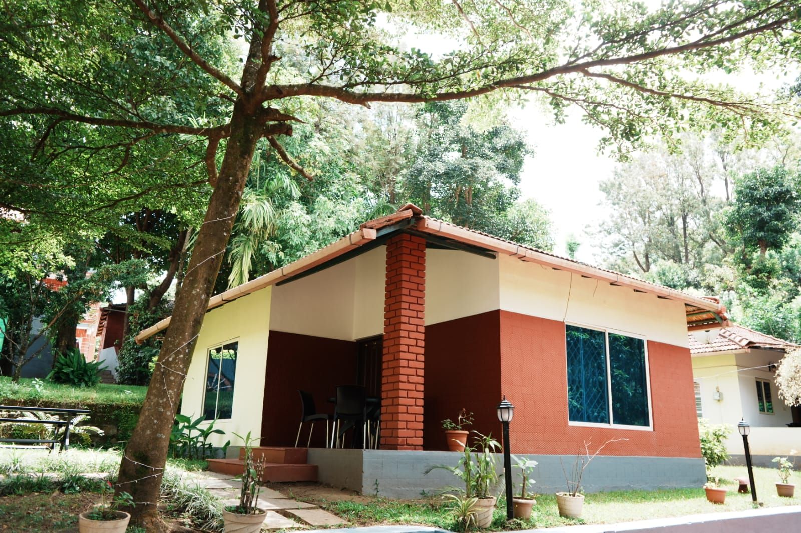 Una casa de una planta con porche, rodeada de árboles y plantas en macetas.
