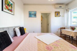 A bedroom with a bed, a bedside table, a chair, a window, and a door leading to a bathroom. - A5 - Cozy Apartment with Pool & Sea View, 2 Min Walk to Beach (Omiš)