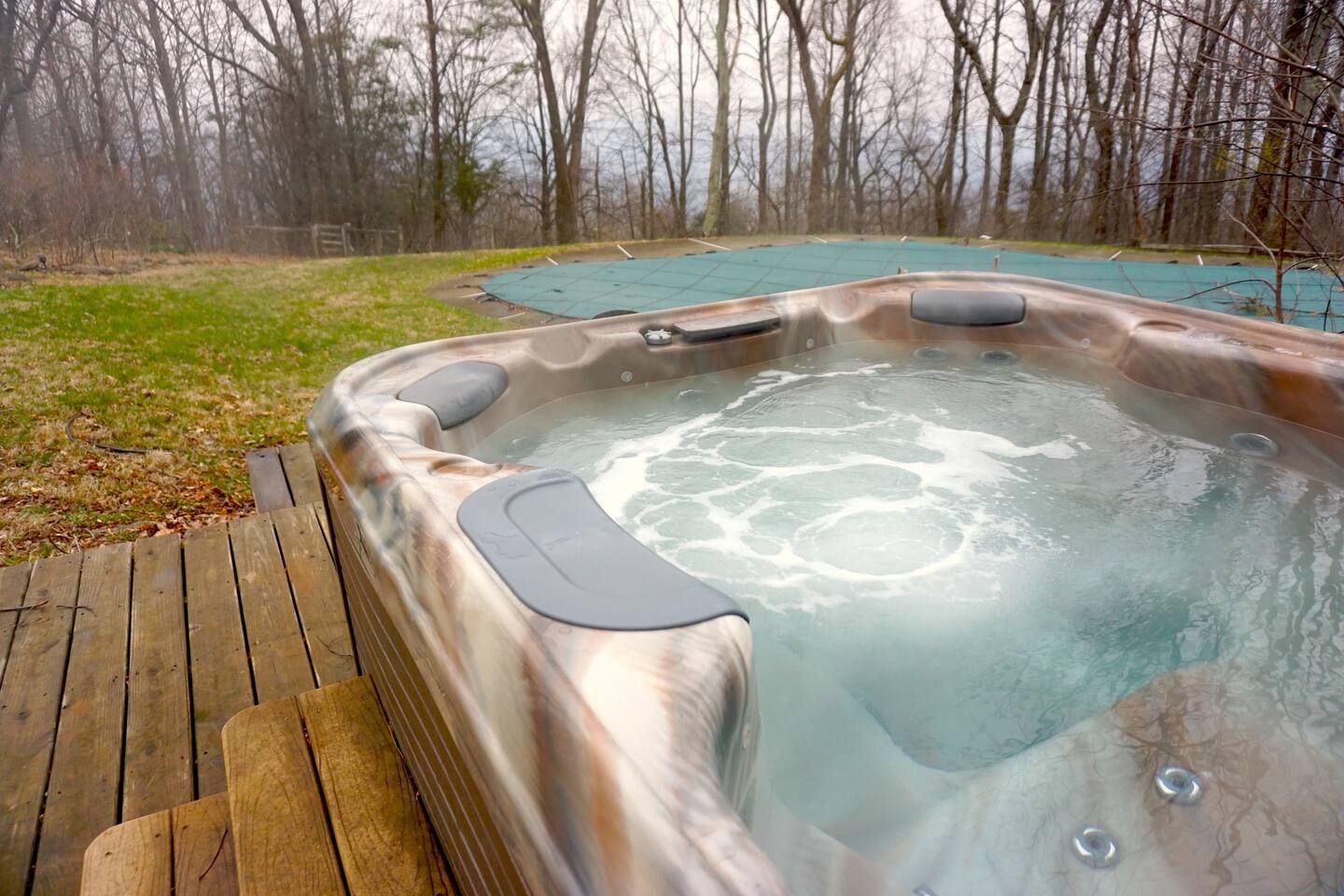 Een hottub met een houten terras en een gazon op de achtergrond.