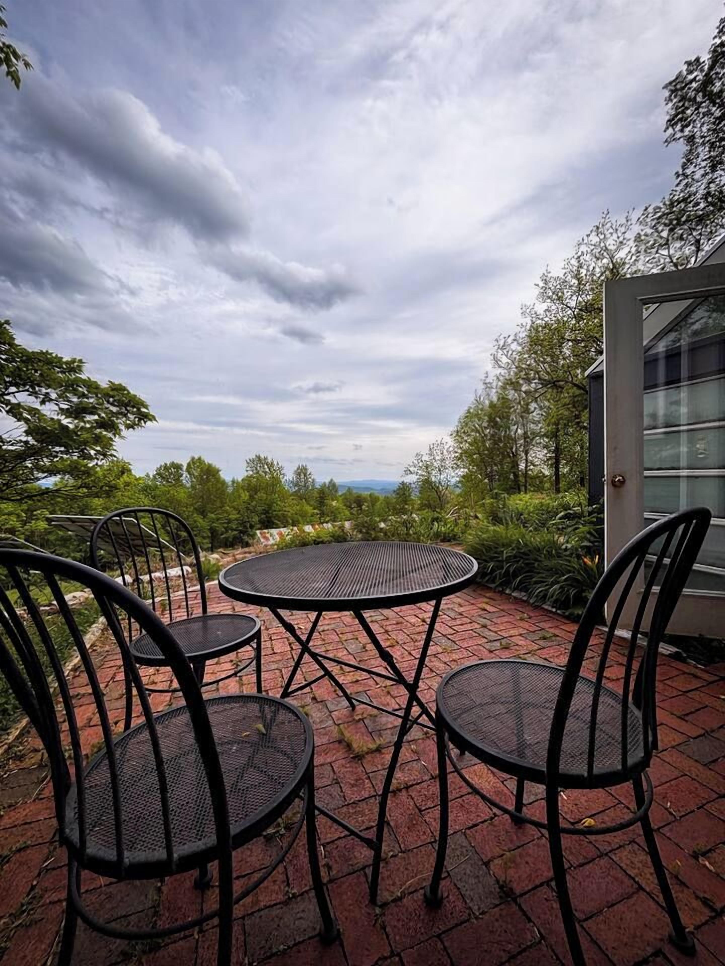 An outdoor patio with a round table and four chairs, surrounded by brick flooring and greenery.