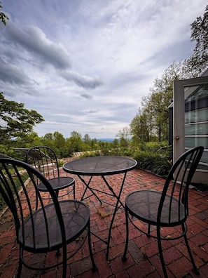 An outdoor patio with a round table and four chairs, surrounded by brick flooring and greenery.