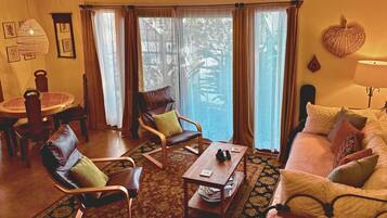 A living room with a sofa, two armchairs, a coffee table, a dining table with chairs, and a large window with curtains.