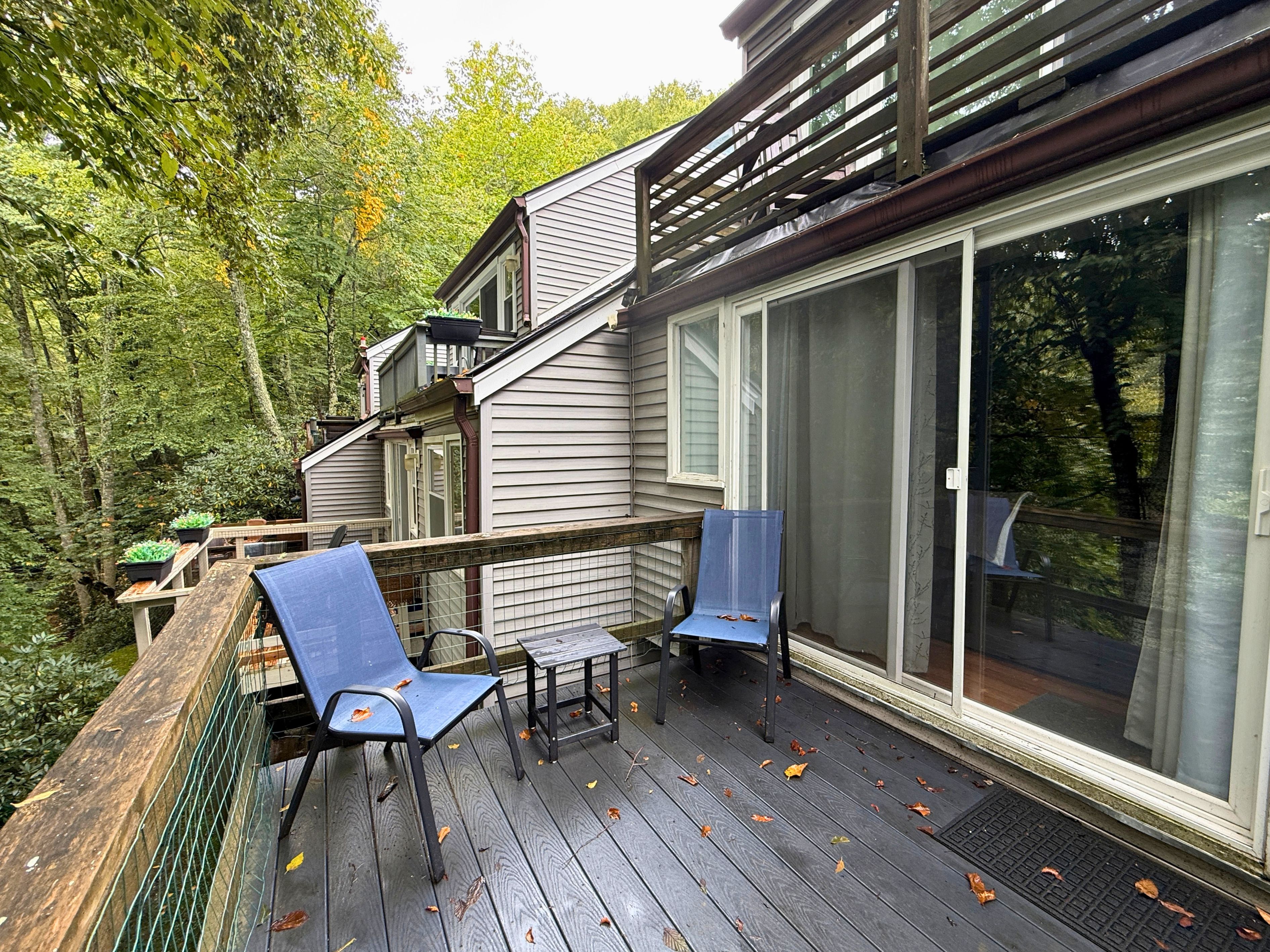 A deck with two chairs and a table, surrounded by a wooden railing, overlooking a forested area.