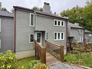 A two-story residential building with a wooden deck leading to a front door. - Freshly Updated Creekside Condo Near Sugar Mountain Resort (Sugar Mountain)