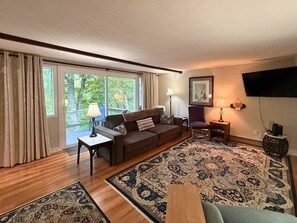 A living room with a sofa, a chair, a coffee table, a TV, and a large window with curtains. - Freshly Updated Creekside Condo Near Sugar Mountain Resort (Sugar Mountain)