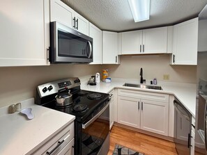 A compact kitchen with white cabinets, a microwave, a stove, and a sink. - Freshly Updated Creekside Condo Near Sugar Mountain Resort (Sugar Mountain)