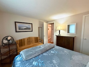 A bedroom with a bed, a wooden bench, a fan, a dresser, a framed picture, and a door leading to another room. - Freshly Updated Creekside Condo Near Sugar Mountain Resort (Sugar Mountain)