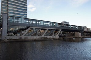 Un pont moderne doté de garde-corps en verre et d’une passerelle piétonne surplombant une étendue d’eau, reliant deux bâtiments.