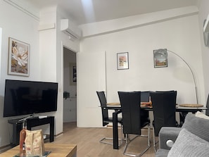 A modern living room with a flat-screen TV, a dining table with chairs, and a sofa. - Charming 2-room apartment in Nice. Comfortable, cozy, and close to the sea (Nice)