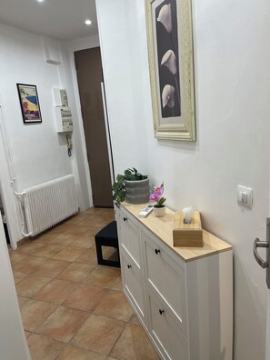 A hallway with a radiator, a potted plant, a framed artwork, and a remote control on a wooden counter. - Charming 2-room apartment in Nice. Comfortable, cozy, and close to the sea (Nice)