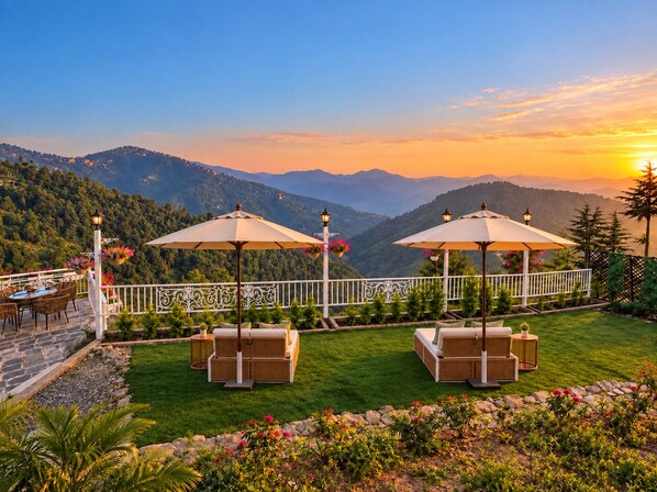 A terrace with outdoor seating, a railing, and a view of a mountainous landscape.