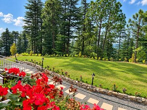 A landscaped garden with a stone pathway, a lawn, and a variety of trees. - La Foret - A Boutique Resort (Shimla)