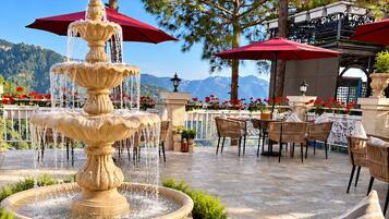 Un espace extérieur aménagé avec des sièges, une fontaine à plusieurs niveaux, des meubles en osier et des parasols rouges.