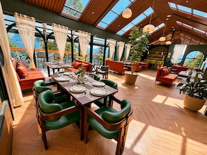 A spacious indoor area with a high ceiling, wooden flooring, and a dining setup with green chairs and a table set for four.