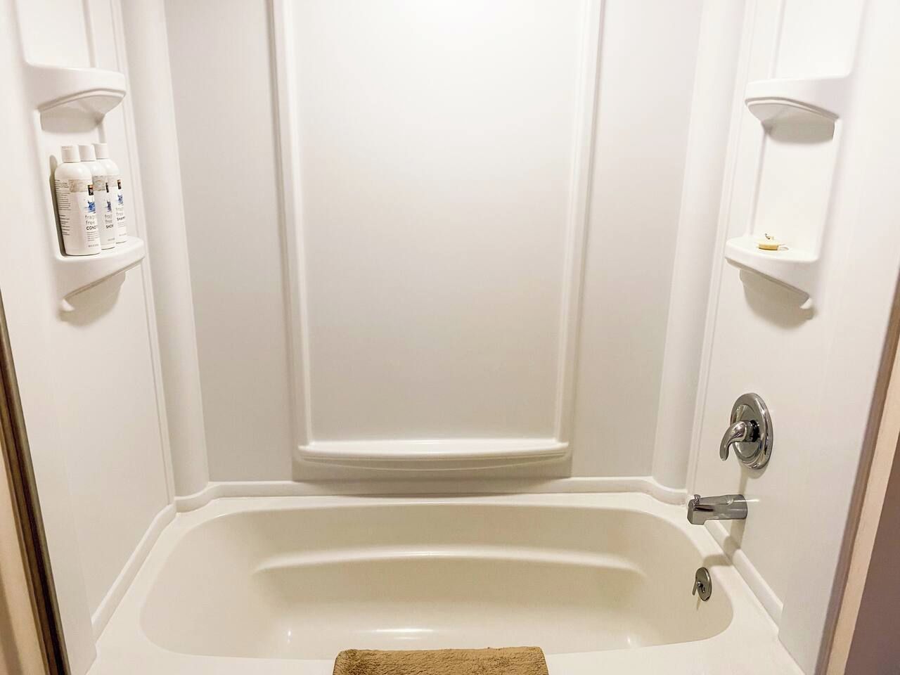 A white bathroom with a bathtub, a shower, and a toilet. There are two shelves with toiletries on the wall.