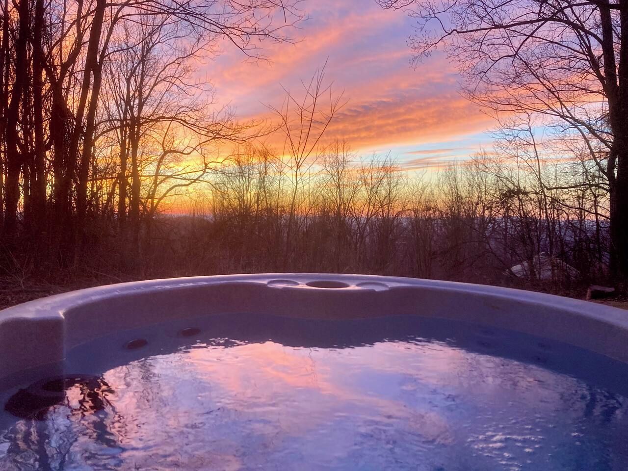 A hot tub surrounded by trees with a sunset in the background.