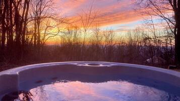 A hot tub surrounded by trees with a sunset in the background.