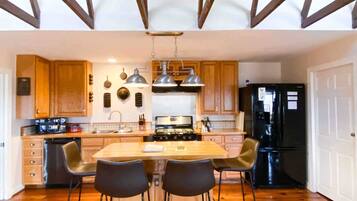 Une cuisine avec des meubles en bois, un îlot central doté de chaises, une cuisinière et un réfrigérateur.