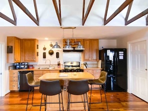 A kitchen with wooden cabinets, a central island with chairs, a stove, and a refrigerator.