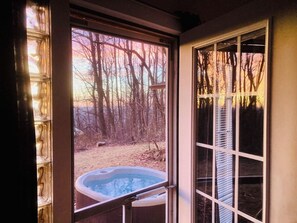 A hot tub outside a house with a view of trees and a clear sky.