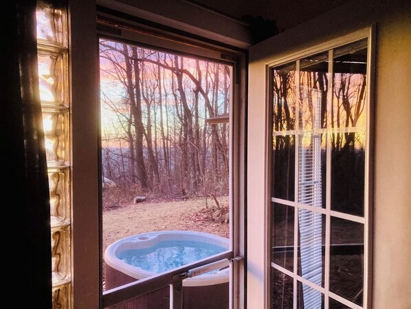 A hot tub outside a house with a view of trees and a clear sky.