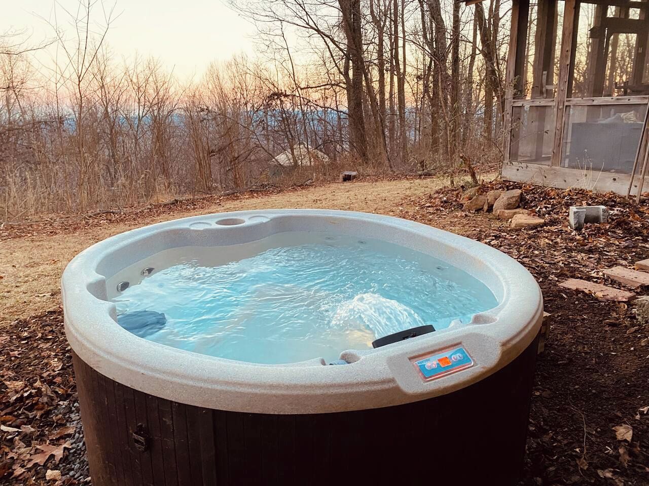A hot tub outdoors surrounded by trees and a wooden structure.