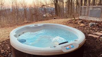 A hot tub outdoors surrounded by trees and a wooden structure.
