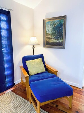 A room with a blue sofa, a wooden side table, a lamp, and a framed painting on the wall.