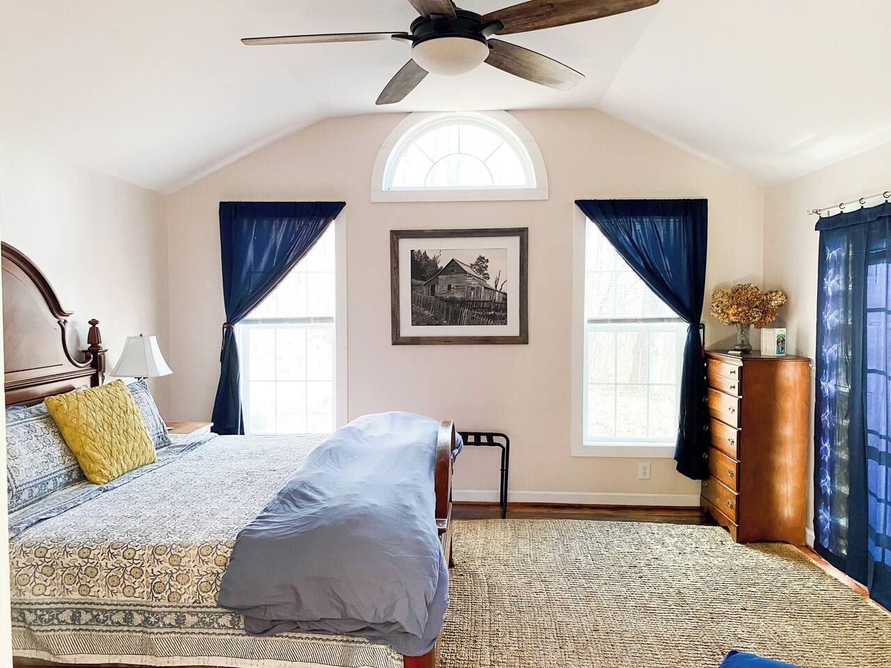 A bedroom with a bed, a ceiling fan, a dresser, and a window with curtains.