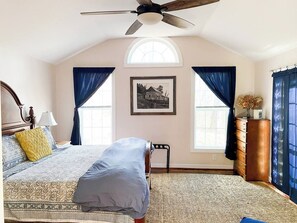 A bedroom with a bed, a ceiling fan, a dresser, and a window with curtains.