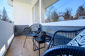 A balcony with wicker furniture, a small table, and a view of the surrounding area. - MY STAY - Relaxation by the Lake with a Sauna & Swimming Pool (Prien am Chiemsee)